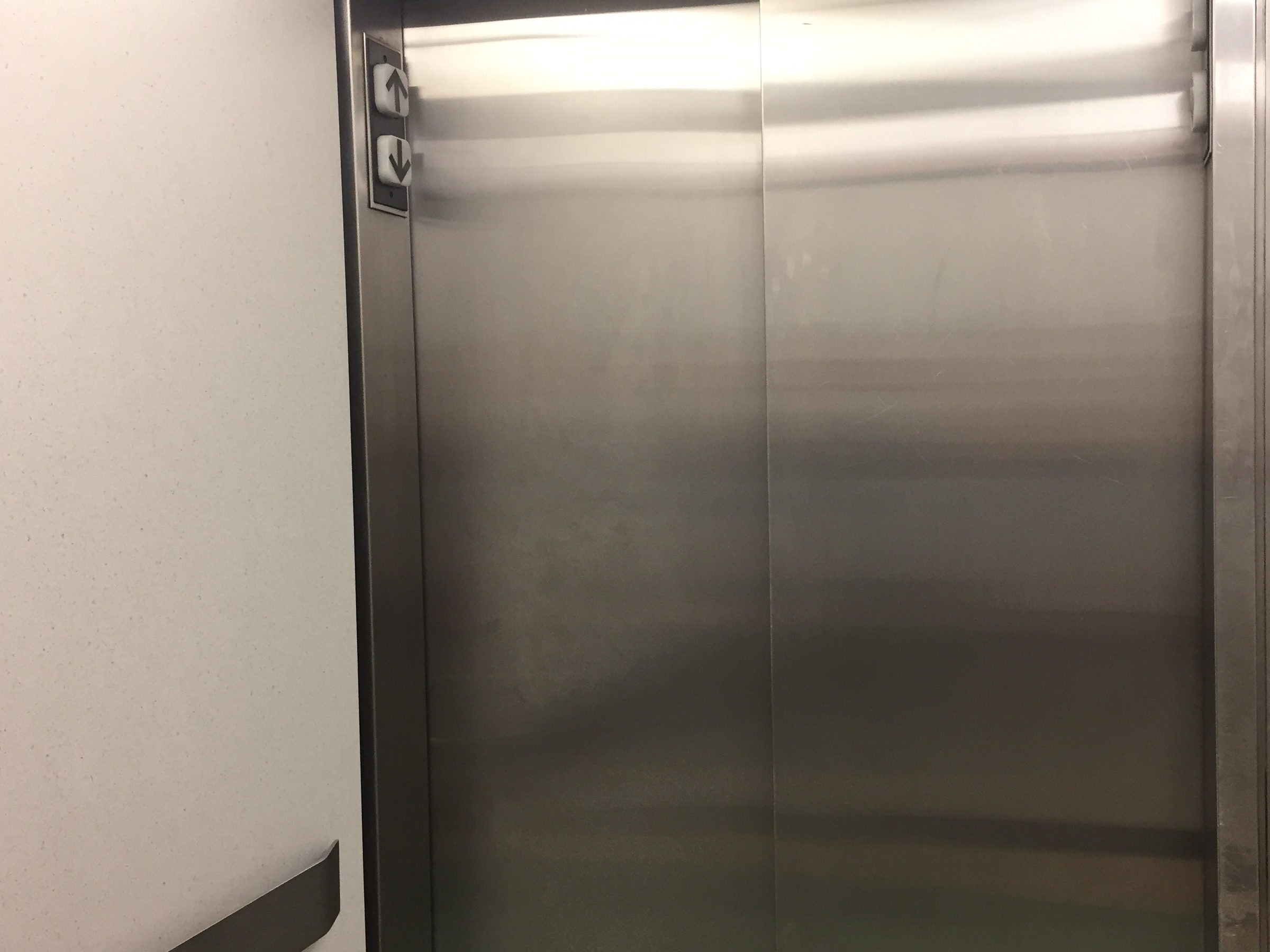 Geschlossene Aufzugstür aus gebürstetem Edelstahl mit Lichtreflexen auf der Oberfläche