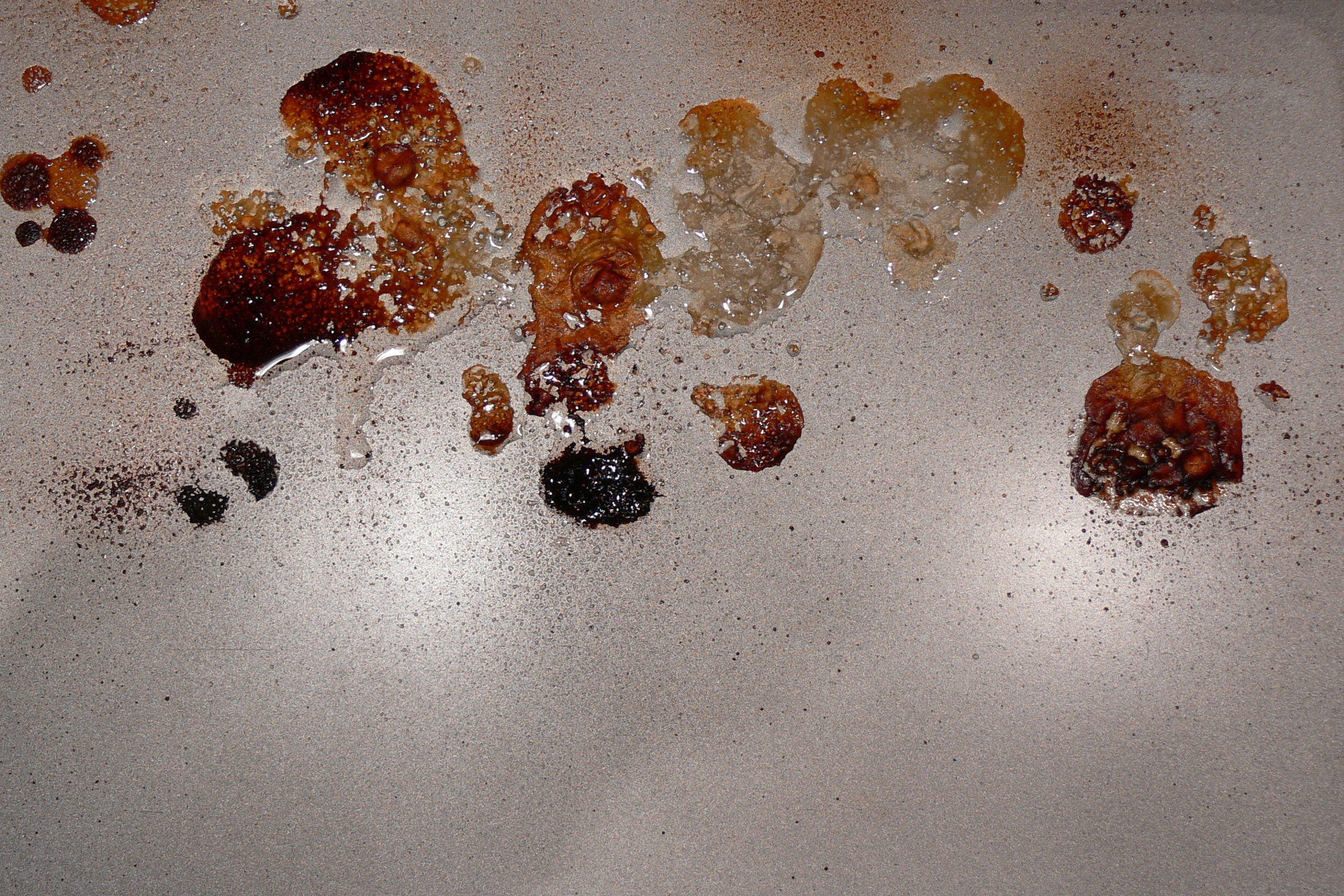 Backblech mit eingebrannten, teils karamellisierten Rückständen und dunklen Krusten neben freien Flächen