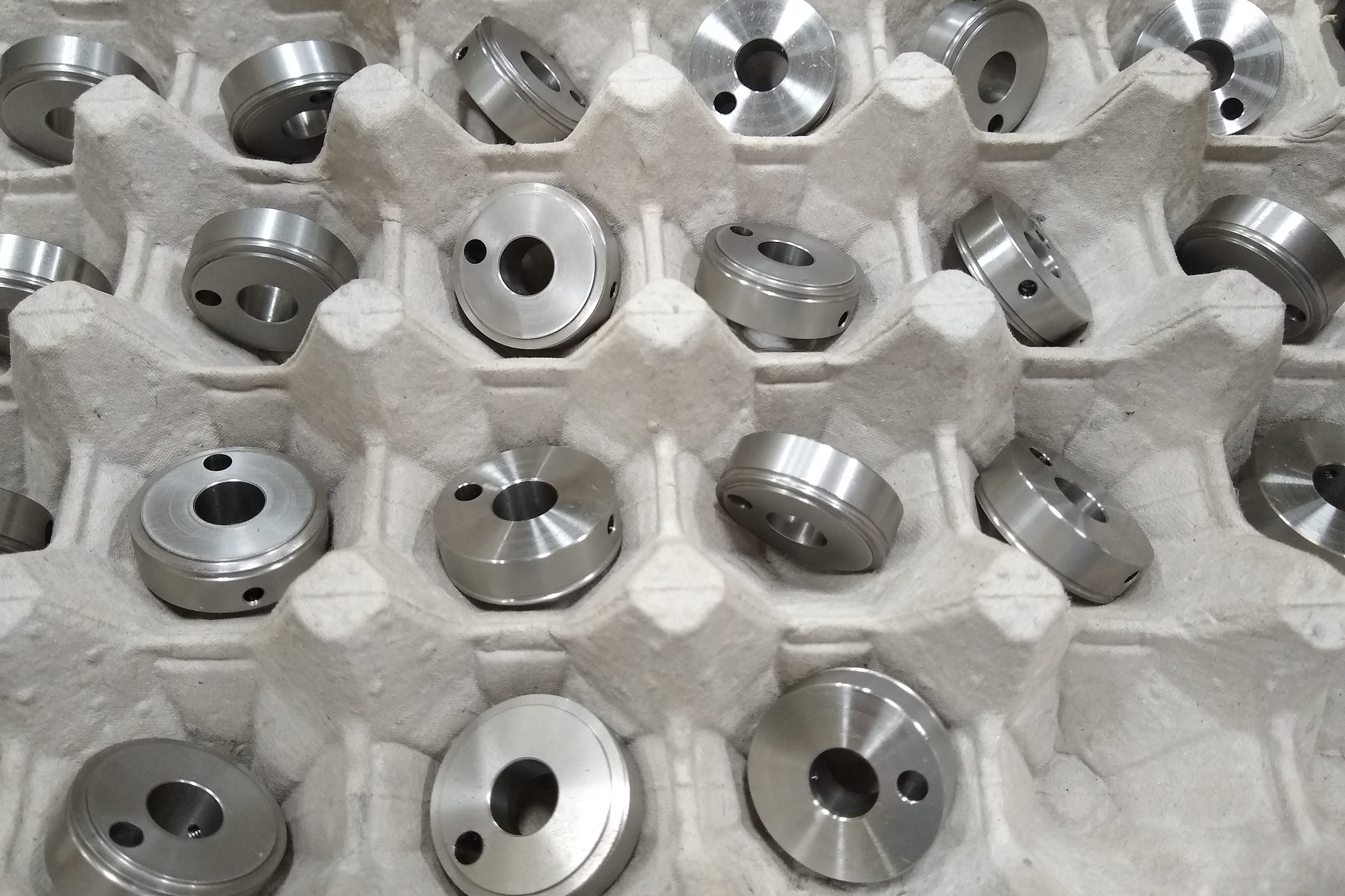 Gleiche gedrehte Metallteile liegen in Reihen in einer Transportpalette aus Pappe