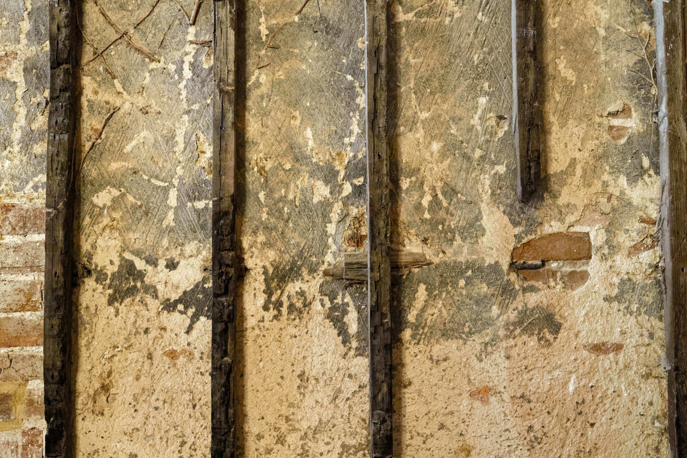 Verrußter, abplatzender Putz zwischen verkohlten Holzständern einer brandgeschädigten Wand