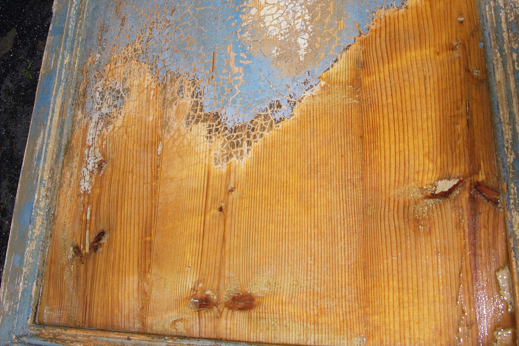 Alte Holztür mit teilweise entfernter blauer Lackschicht, darunter liegt das Holz frei