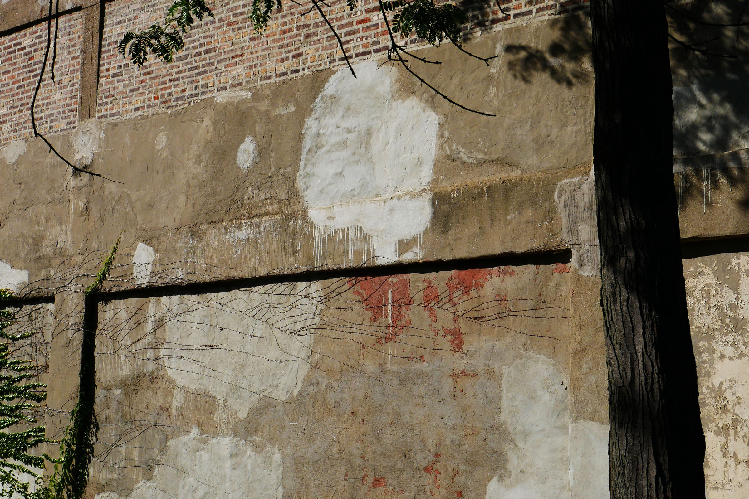 Verputzte Wand mit vielen ungleichen, überstrichenen Flecken und roten Farbresten früherer Graffiti
