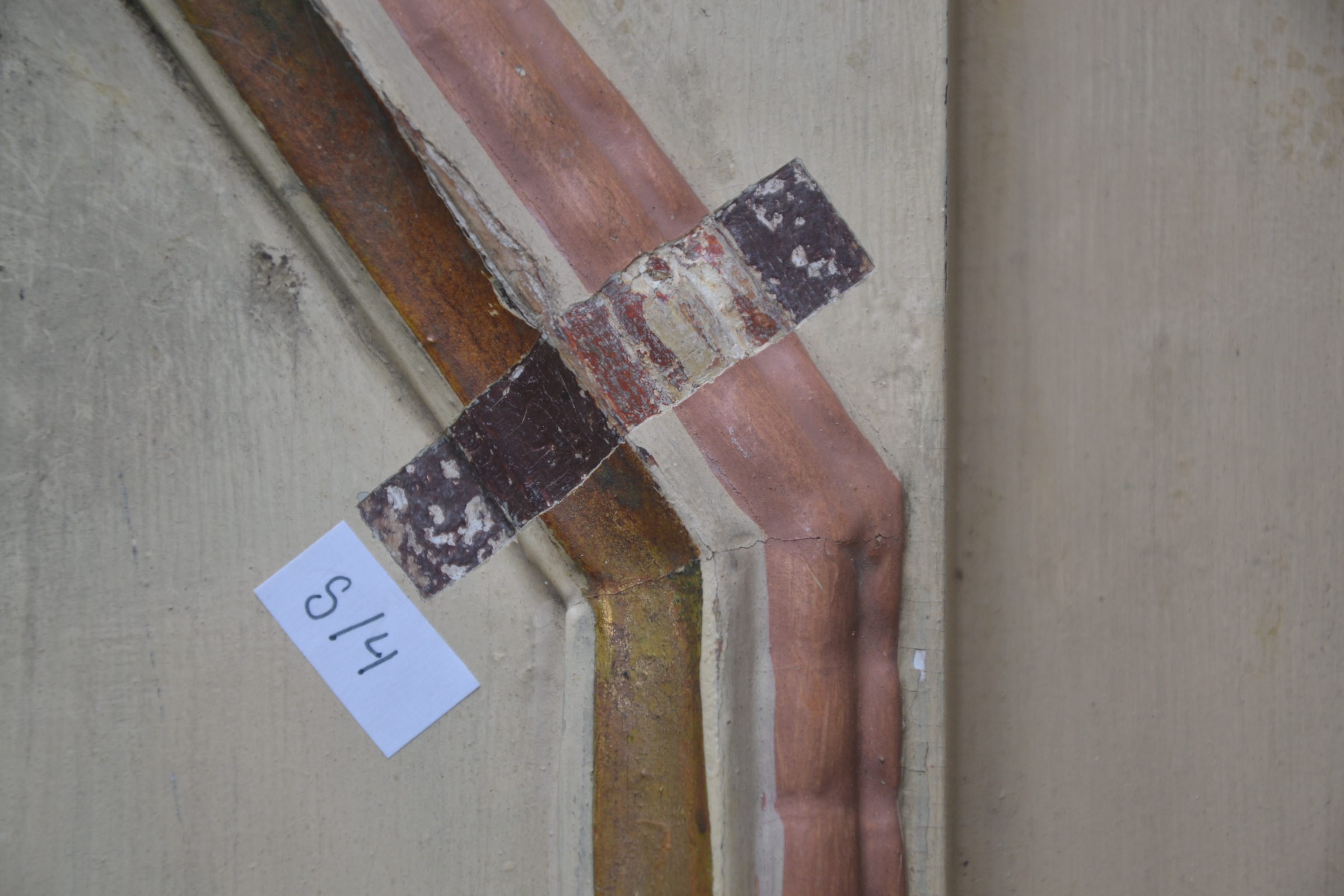 Profilleiste aus Holz mit freigelegtem Probefenster, in dem mehrere Farbschichten übereinander sichtbar sind