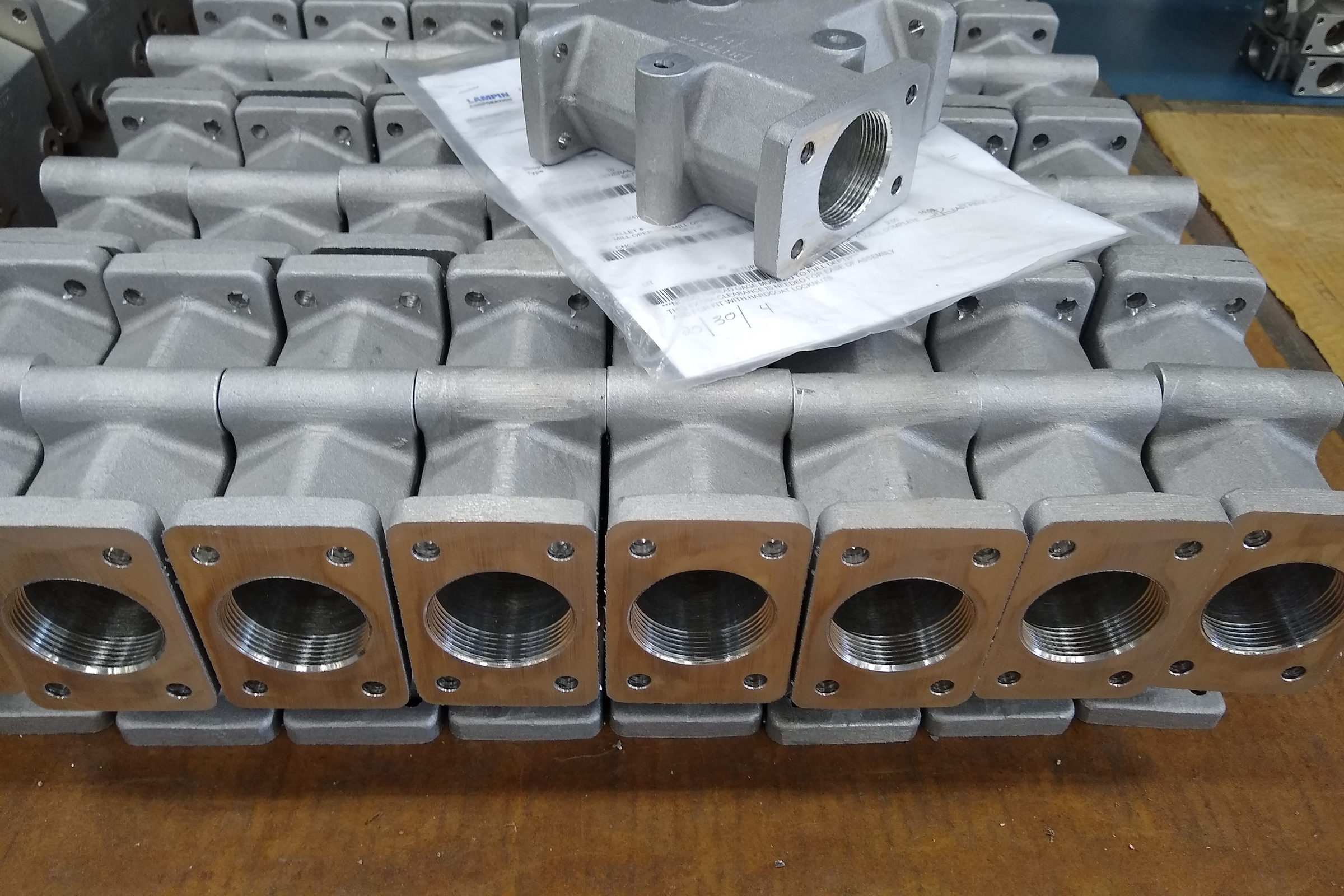 Viele gleiche Gehäuse aus Aluminiumguss in Reihen auf einer Palette, obenauf ein Teil auf einem Begleitschein