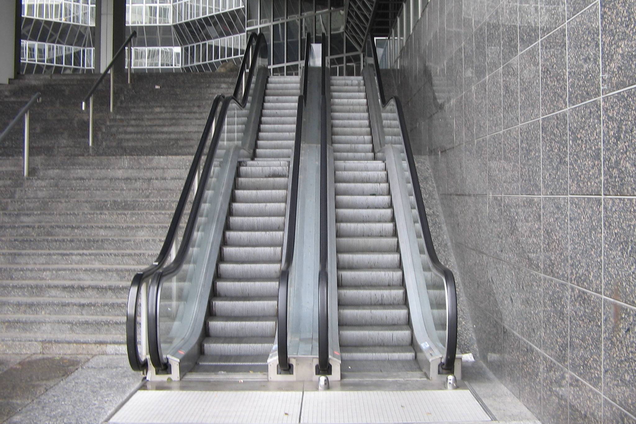 Zwei Rolltreppen neben einer Steintreppe mit gut erkennbaren Stufen, Kammplatten, Seitenverkleidungen und Handläufen