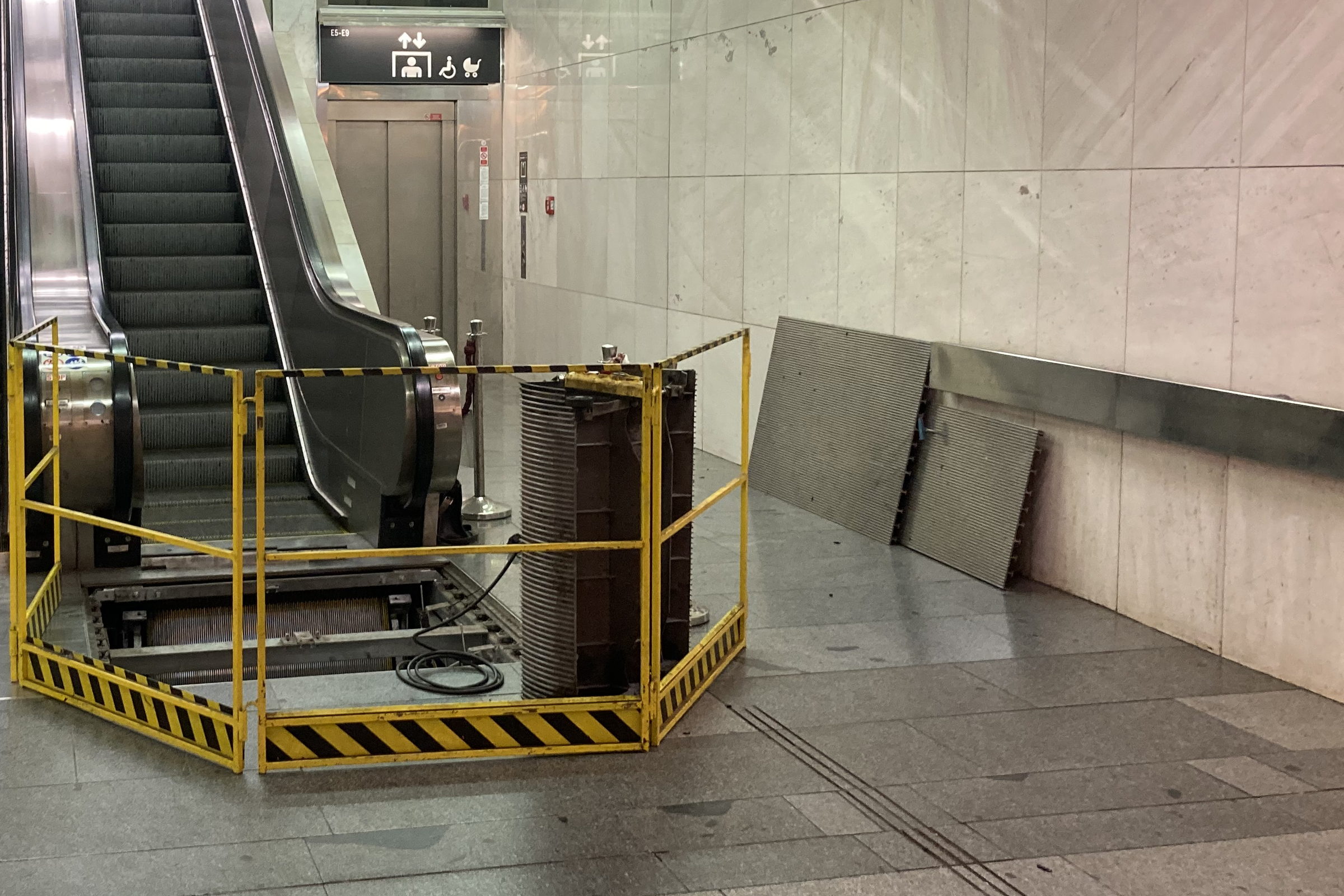 Rolltreppe in einer U-Bahn-Station, an ihrem Fuß ist eine geöffnete Bodenöffnung mit einem gelben Gitter abgesperrt