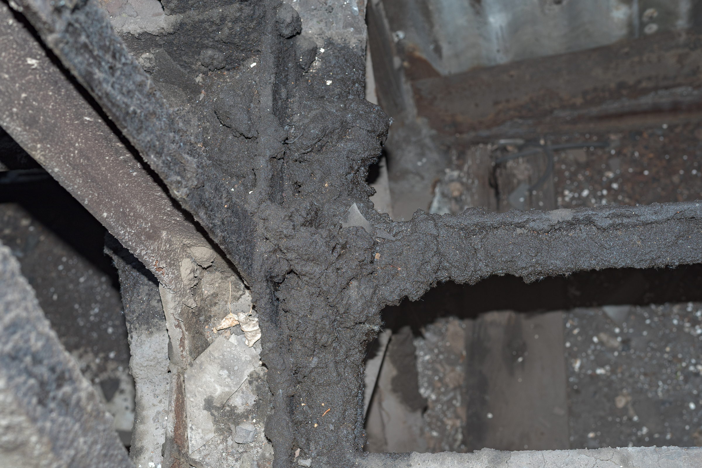 Dicke Rußablagerung auf Stahlträgern und dem angrenzenden mineralischen Untergrund in einem Maschinenhaus