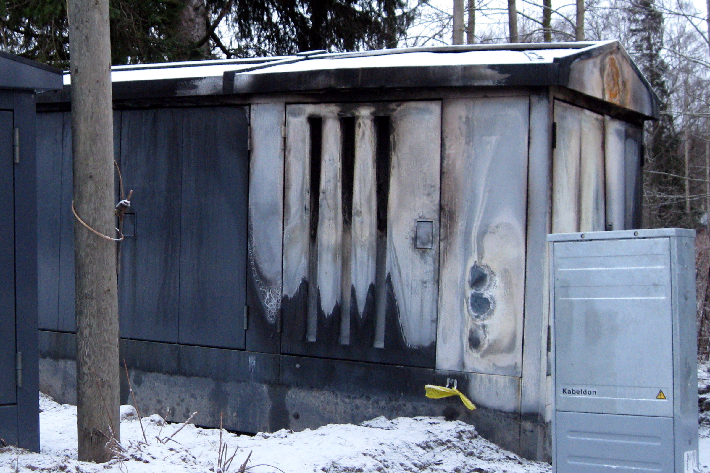 Lackiertes Metallgehäuse einer Trafostation mit Rußfahnen und hitzegeschädigter Beschichtung