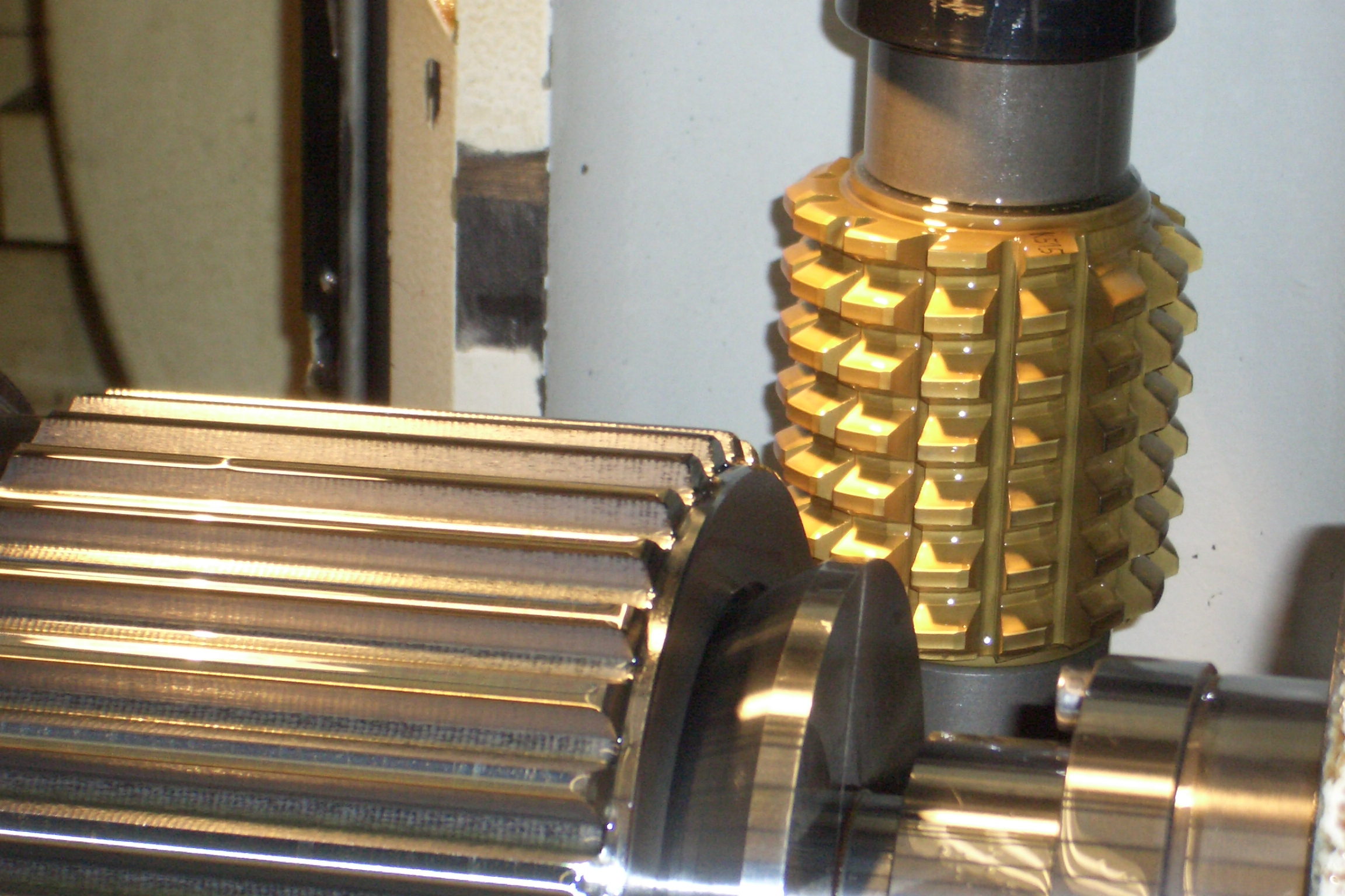 Goldfarben beschichteter Wälzfräser in einer Verzahnungsmaschine neben einer gefrästen Welle