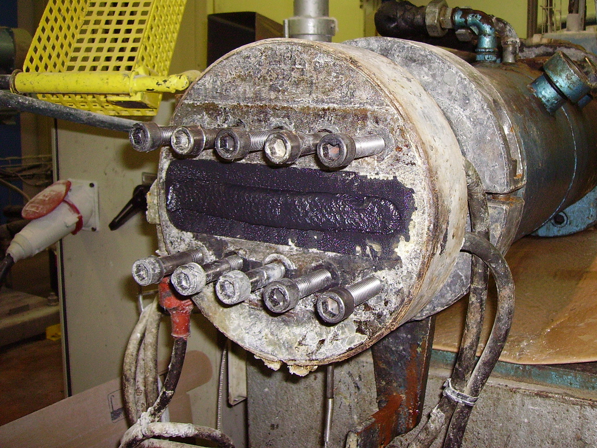 Extrusionswerkzeug an einer Kunststoffanlage mit verkrusteten Ablagerungen rund um Austrittsspalt und Schrauben