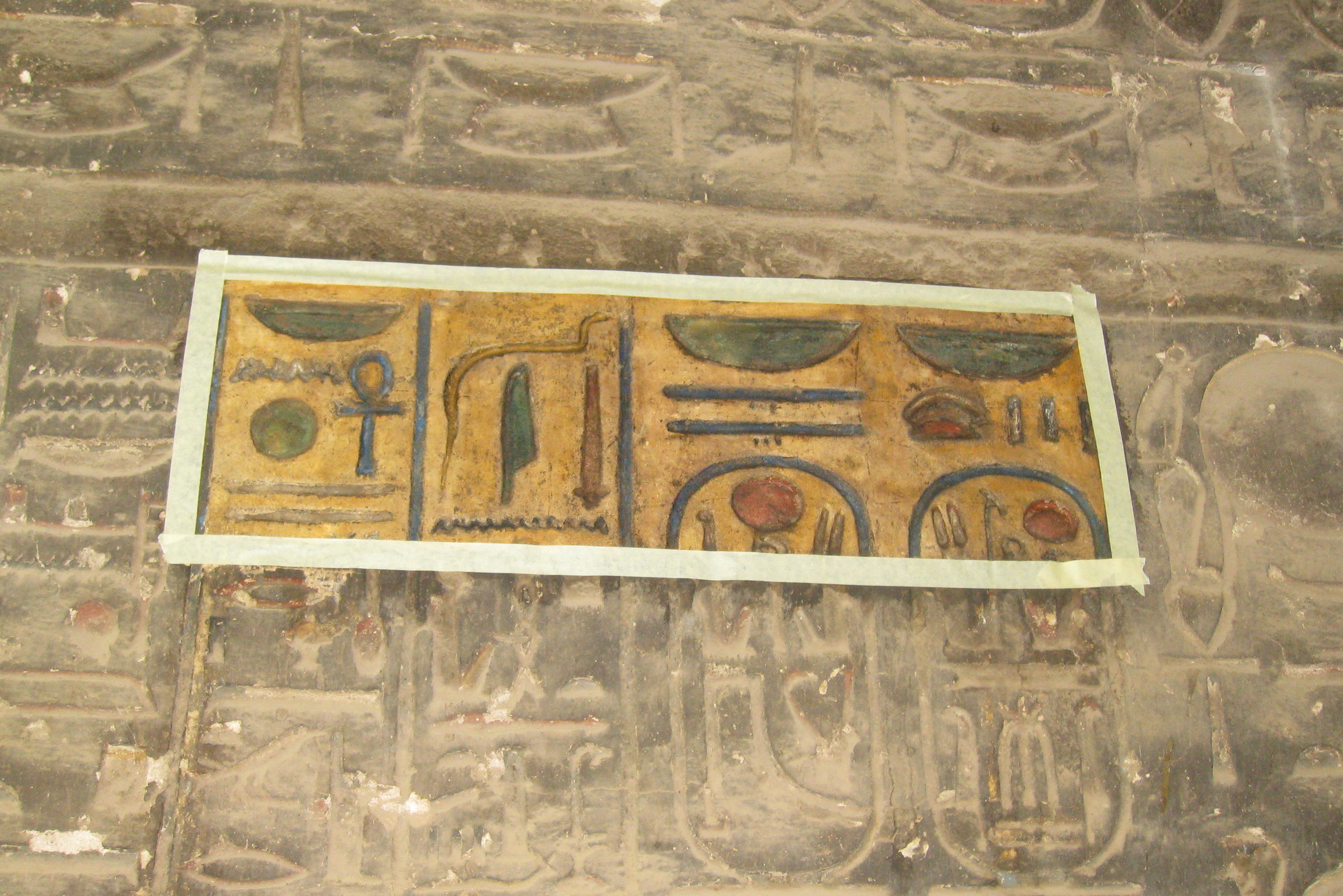 Mit Klebeband abgegrenztes, gereinigtes Probefeld auf einer stark verrußten Wand mit Hieroglyphen-Relief.