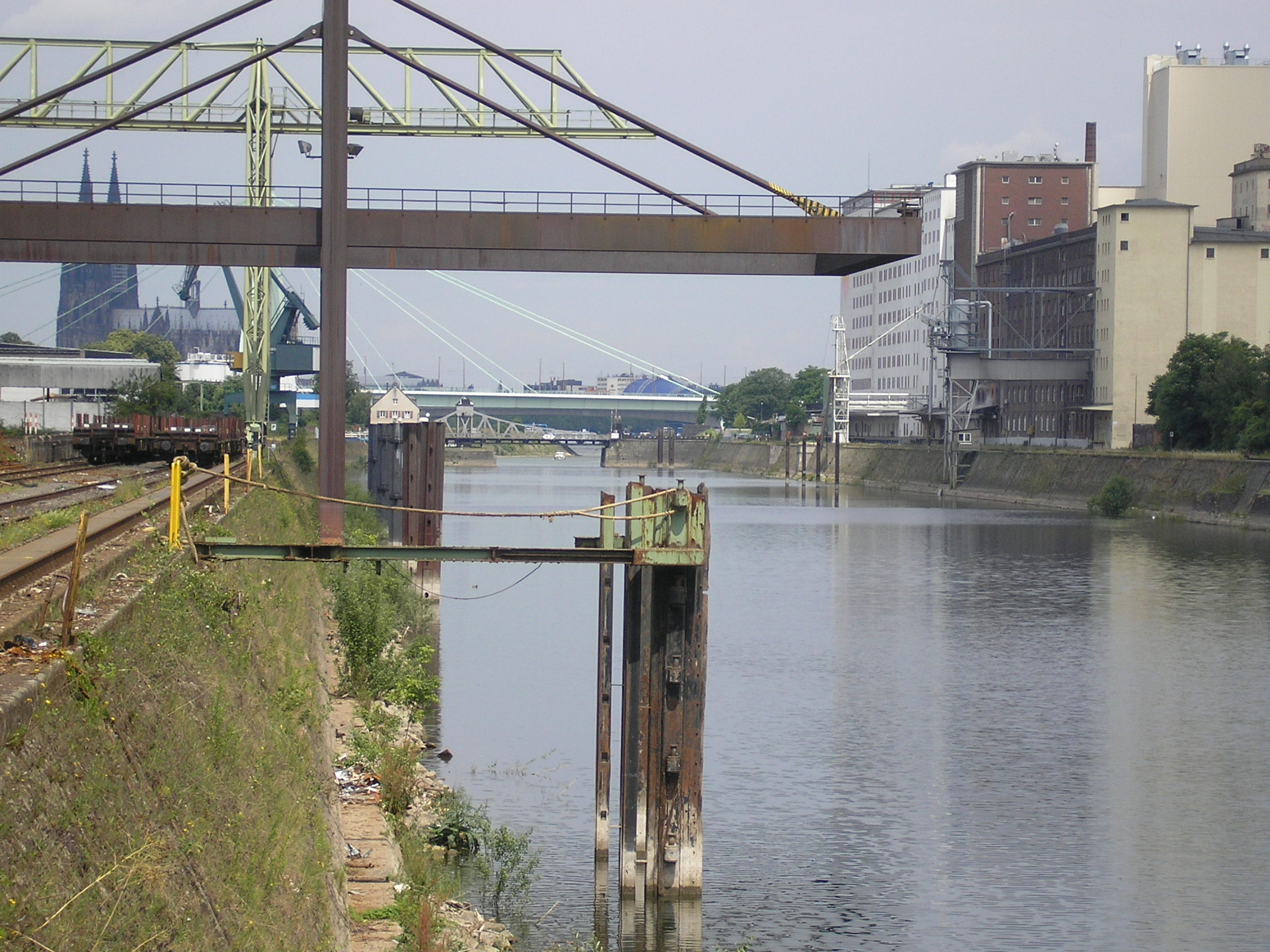 Hafenbecken des Deutzer Hafens mit Kranbrücke, Gleisen und Industriegebäuden, im Hintergrund der Kölner Dom.